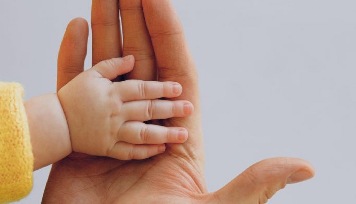 crop-person-touch-palms-with-newborn-baby-on-gray-backdrop-3845458