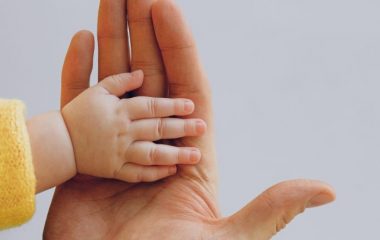 crop-person-touch-palms-with-newborn-baby-on-gray-backdrop-3845458